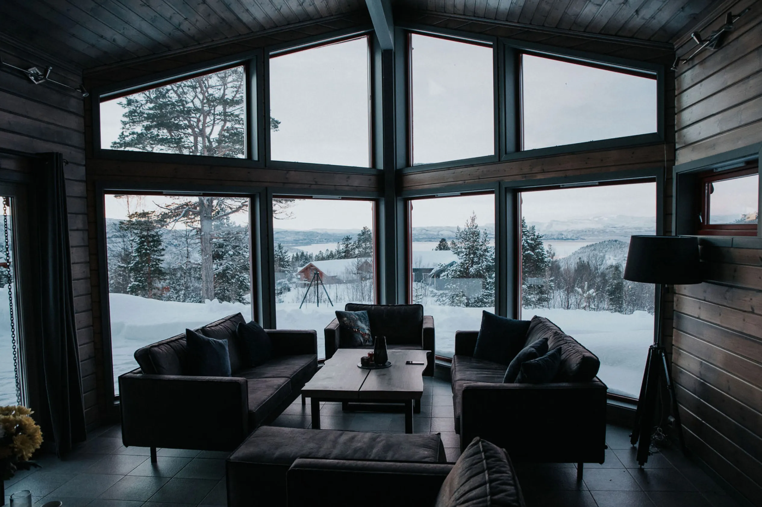 Storstua på Alten Lodge med sofaer og panoramavinduer mot fjorden
